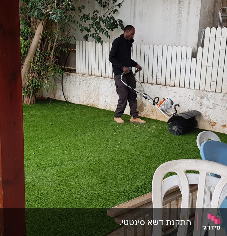 אדם משתמש במכונת ניקוי דשא סינתטי בגינה